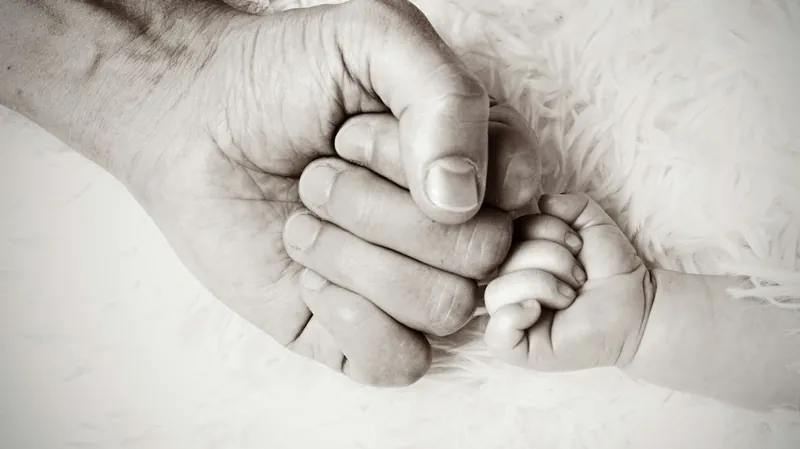 An adult's fist bumping a baby's fist